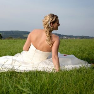 Braut in Hochzeitskleid sitzt auf grüner Wiese