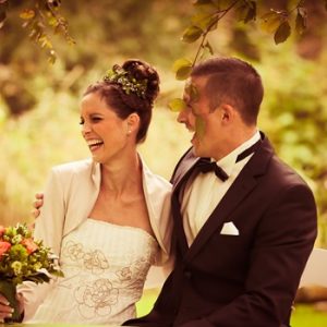 Braut mit Hochsteckfrisur und Brautstrauß neben Brautigam in schickem Anzug